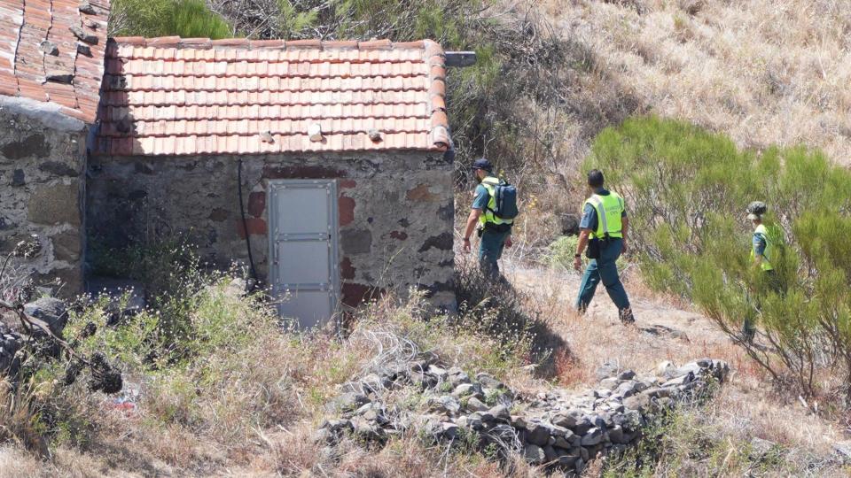 Two officers from the Guardia Civil search on a trail near a rustic building