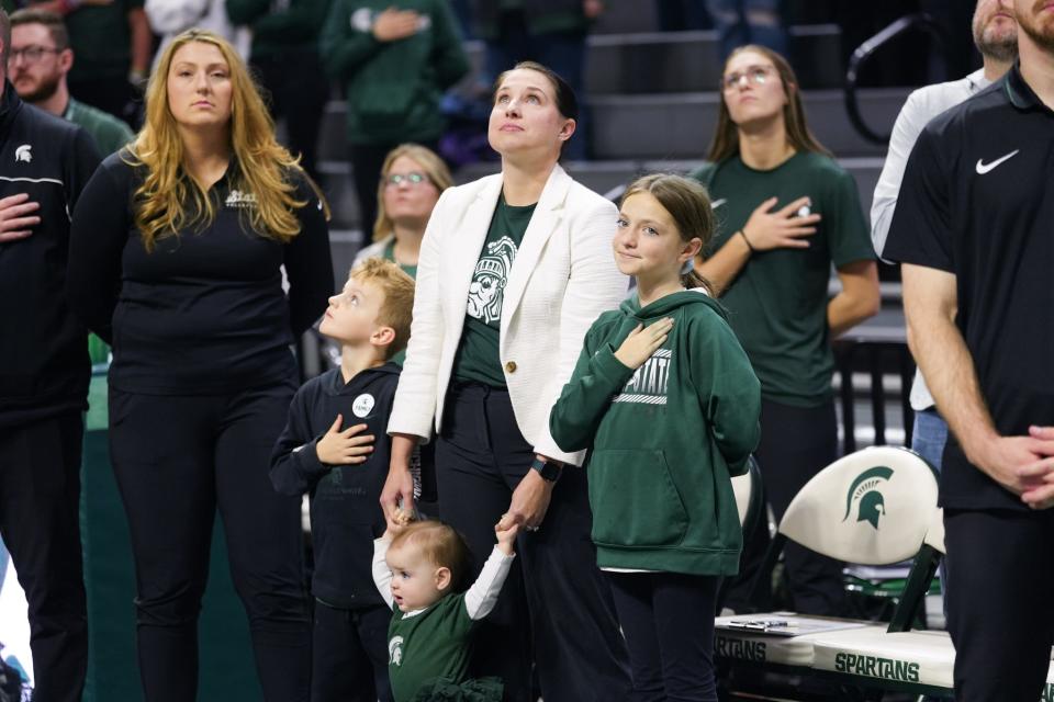 MSU volleyball coach Leah Johnson stands with her children, Edith, right, Roz, center, and PJ during the national anthem before a volleyball match last season at Breslin Center.
