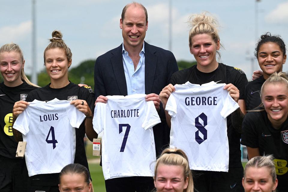 Prince William, Duke of Cambridge (C) poses with the England's football jersey bearing the names of his three children and with the England's women football team players during a visit at their training centre