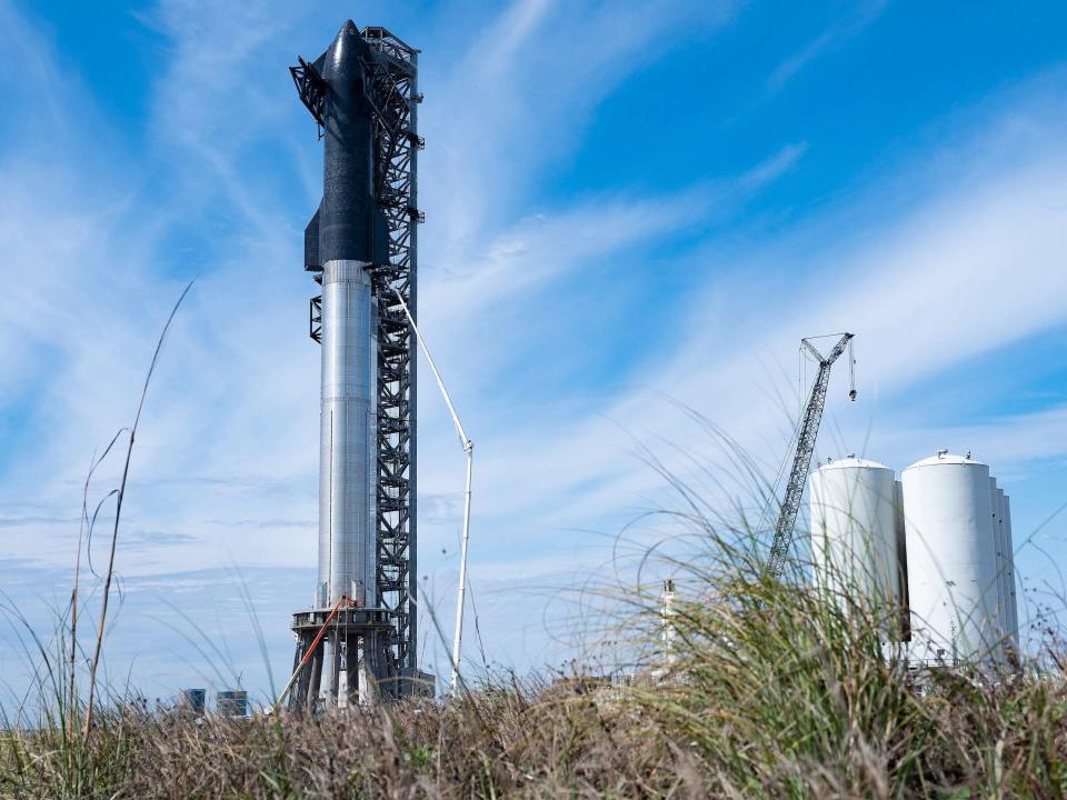 black starship rocket stacked atop silver super heavy boost on flat texas plain against blue skies