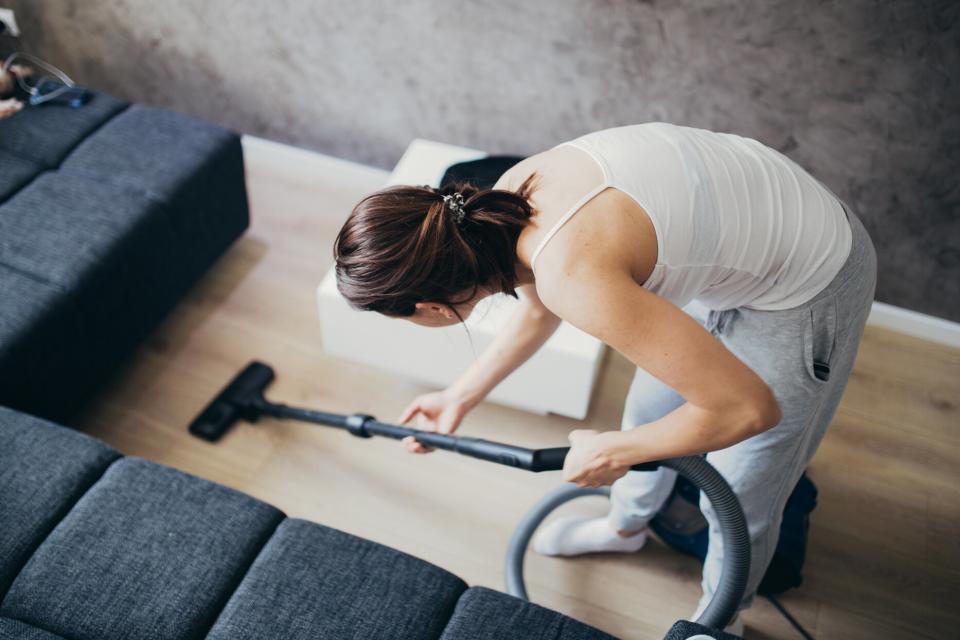 person vacuuming hard wood floor next to couch