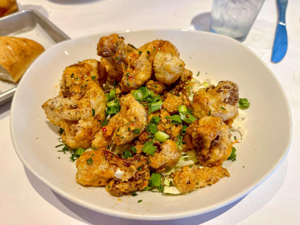 A white bowl filled with scallions and breaded cauliflower pieces on a white tablecloth