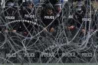 Police stand guard behind barbed wire barricading the base entrance of the 11th Infantry Regiment, a palace security unit under direct command of the Thai king, as they await for the arrival of protesters Sunday, Nov. 29, 2020 in Bangkok, Thailand. Pro-democracy demonstrators are continuing their protests calling for the government to step down and reforms to the constitution and the monarchy, despite legal charges being filed against them and the possibility of violence from their opponents or a military crackdown. (AP Photo/Sakchai Lalit)