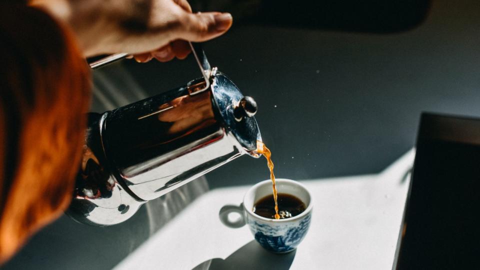 a cup of coffee being filled from a stainless steel french press