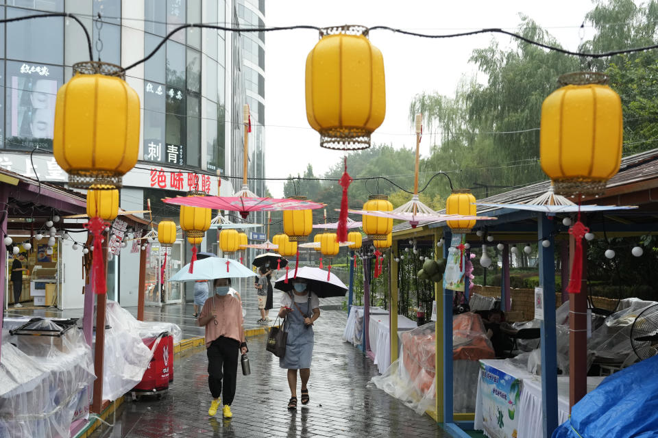 Residents cover up with umbrellas as they walk past stalls closed during a rainy day in Beijing, Sunday, Aug. 14, 2022. (AP Photo/Ng Han Guan)