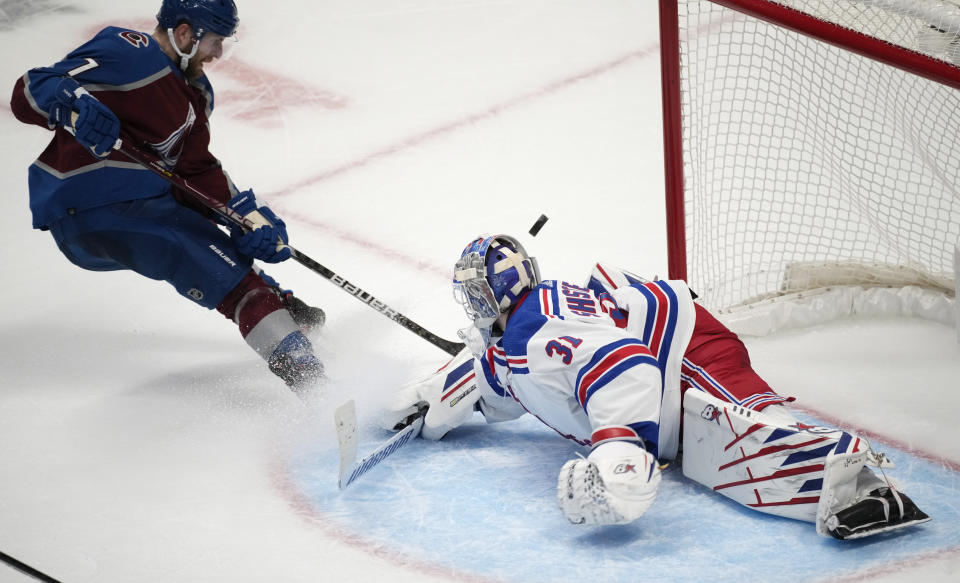 New York Rangers goaltender Igor Shesterkin, right, deflects a shot by Colorado Avalanche defenseman Devon Toews in overtime of an NHL hockey game Friday, Dec. 9, 2022, in Denver. (AP Photo/David Zalubowski)