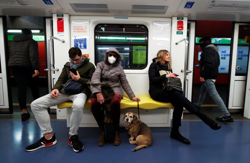 A woman wearing a protective mask and her dog sit on the subway in Milan