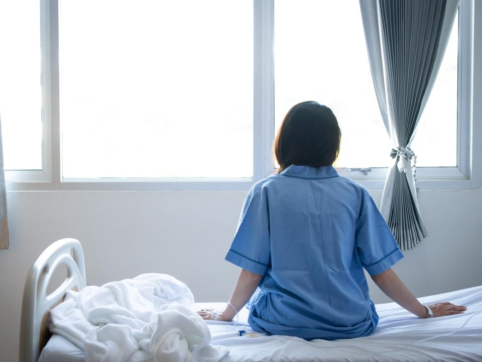 Back view of patient woman sitting on bed in hospital ward