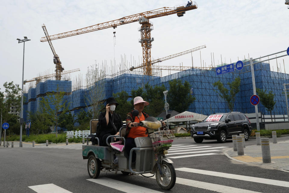 FILE - Residents on a tricycle ride past a car with a sign that reads, "Country Garden homeowners rights protections car," parked near homeowners camping outside the Country Garden One World City project under construction on the outskirts of Beijing on Aug. 17, 2023. (AP Photo/Ng Han Guan, File)