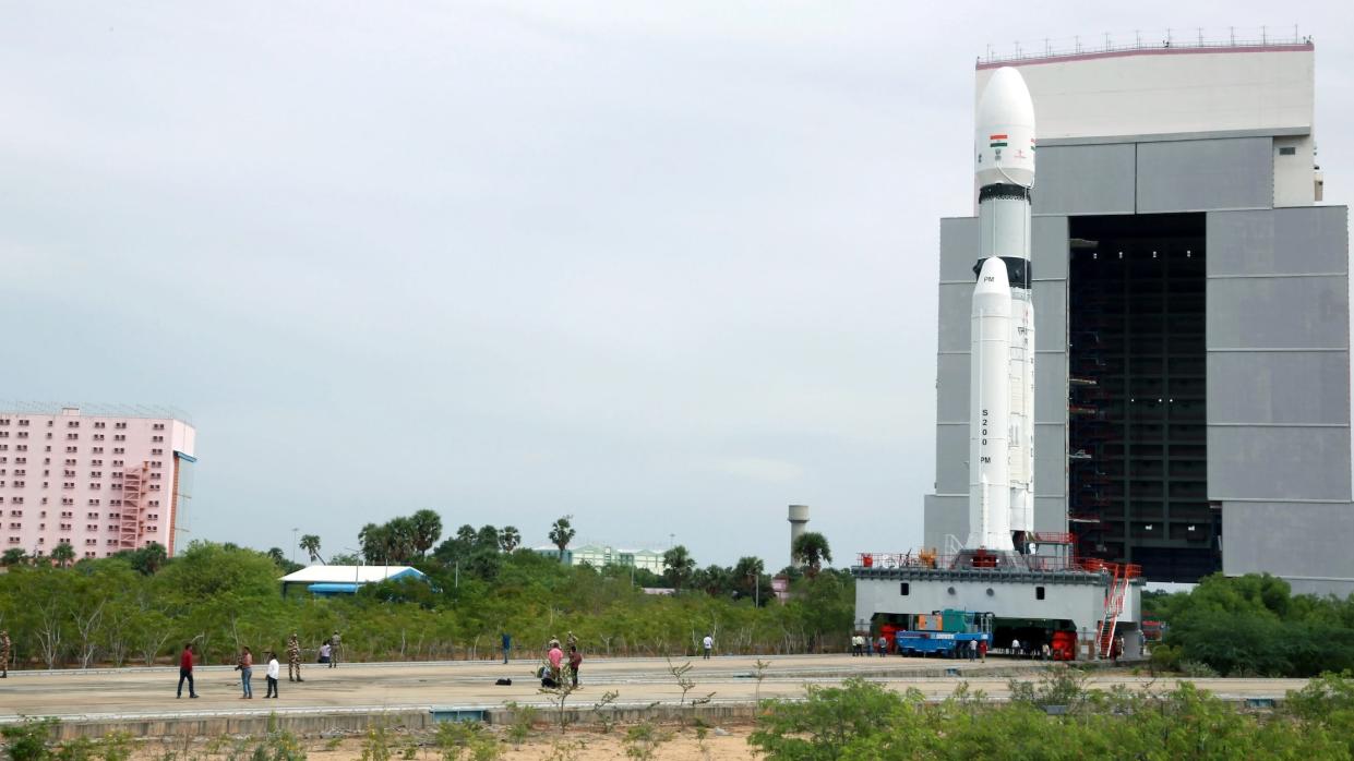  a white rocket rolls out of a large building toward its launch pad 