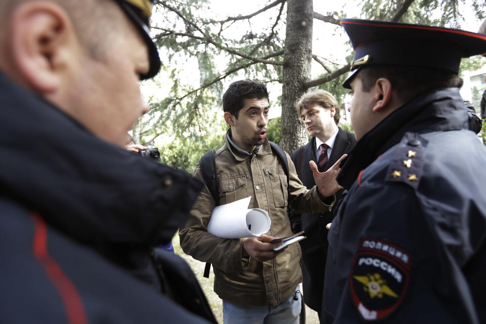 Activist David Khakim, center, talks to police officers after pulling out a banner protesting a recent prison sentence for a local environmentalist in front of the Olympic rings, Monday, Feb. 17, 2014, in central Sochi, Russia. Khakim was holding a one-man picket outside the city administration in central Sochi on Monday when two police officers took him away. Russia passed an ad-hoc law last year, banning public gatherings and rallies in Sochi during the Olympics. One-man pickets, however, are not covered by this law. Khakim was protesting the three-year prison sentence given last week to environmental activist Evgeny Vitishko for spray-painting a fence on a property in a forest where construction is banned. (AP Photo/David Goldman)