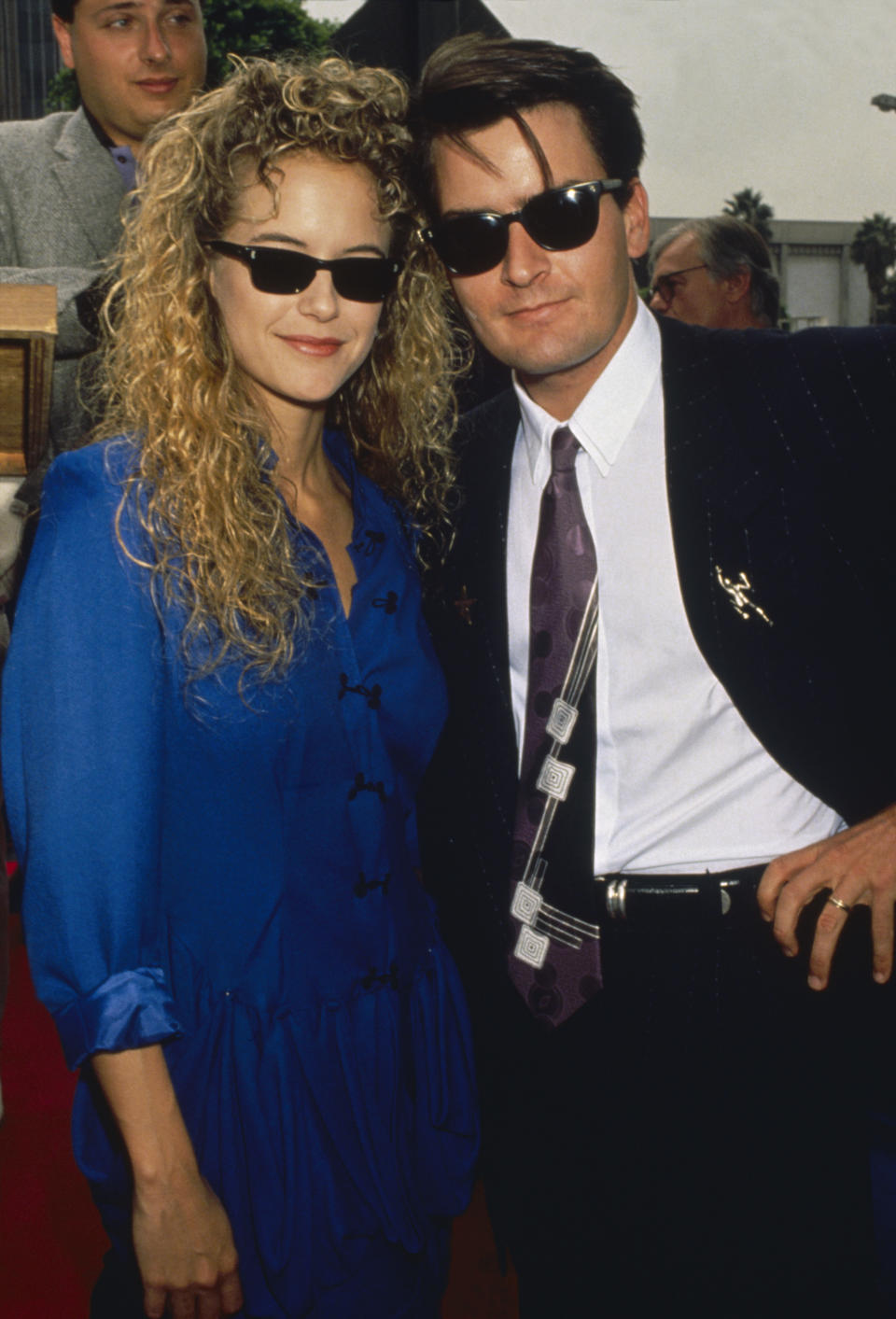 A young Charlie Sheen and Kelly Preston on the red carpet; they're both wearing sunglasses