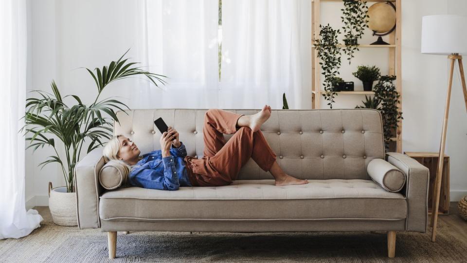 young woman using mobile phone lying on sofa at home