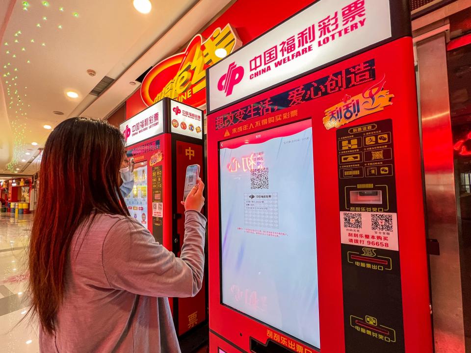 A woman buys a ticket on a vending machine of China Welfare Lottery in a shopping machine in Zhengzhou city in central China's Henan province Thursday, April 14, 2022.