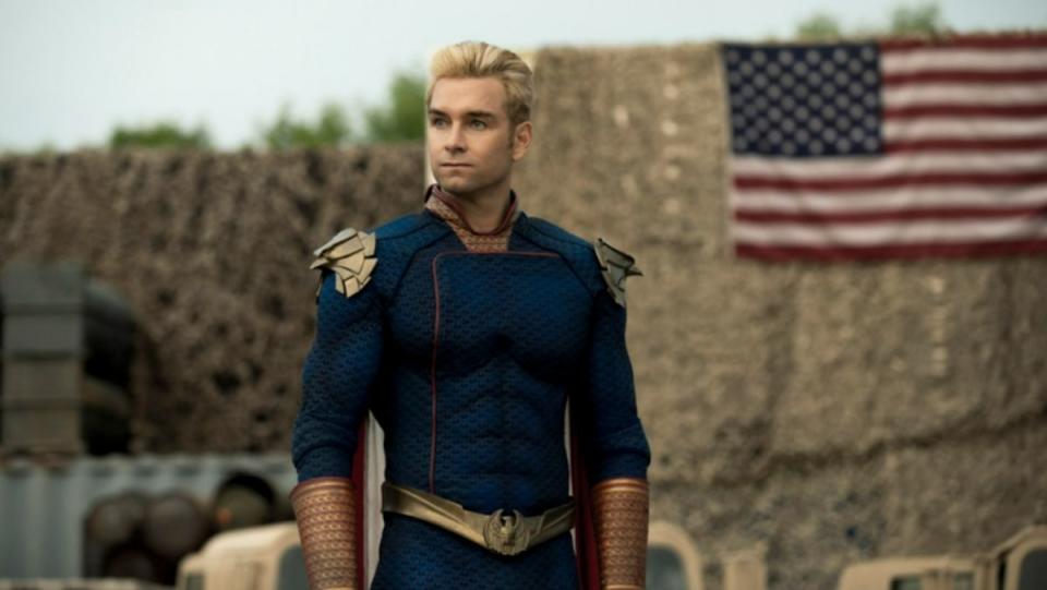 photo of Homelander standing in front of American flag wearing his costume