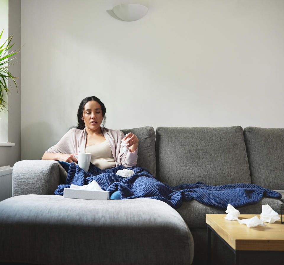 Woman on the couch with a cup of tea and a box of tissues on a sick day