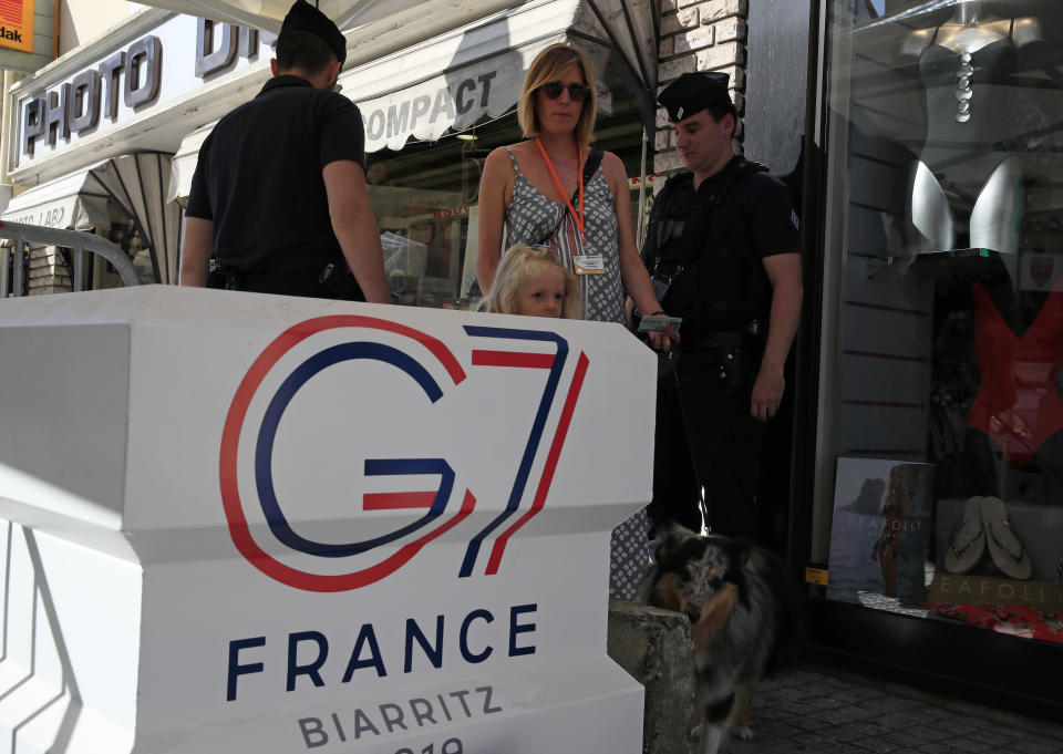 A woman with her family walks past police officers inside the restricted area ahead of the G-7 summit in Biarritz, France Friday, Aug. 23, 2019. U.S. President Donald Trump will join host French President Emmanuel Macron and the leaders of Britain, Germany, Japan, Canada and Italy for the annual G-7 summit in the elegant resort town of Biarritz. (AP Photo/Peter Dejong)