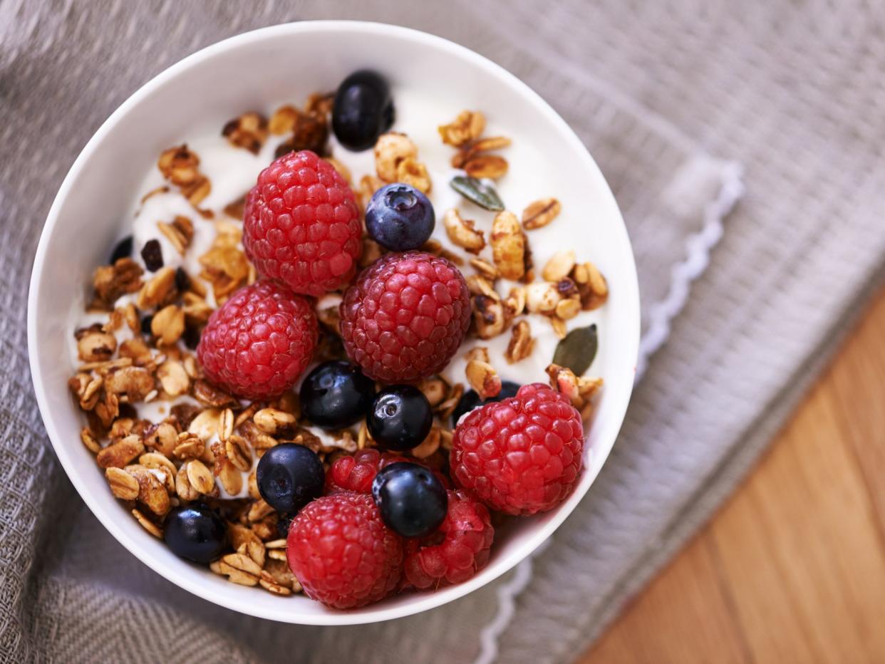 High angle shot of granola, yoghurt and berries in a bowl on a tabletop.