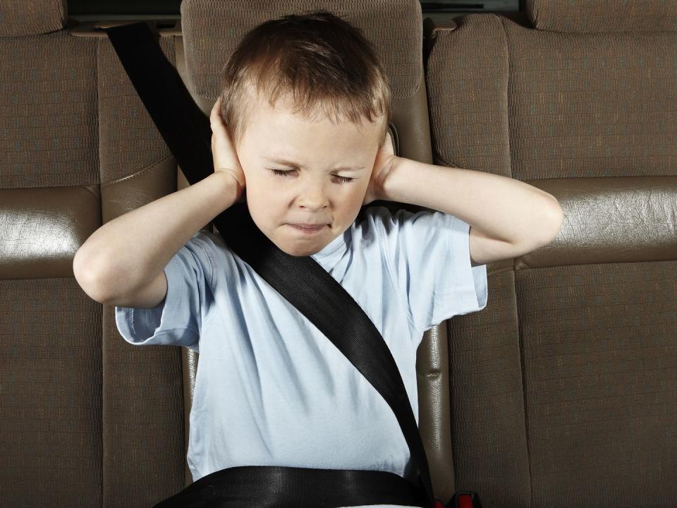 boy in car with eyes closed, hands covering ears