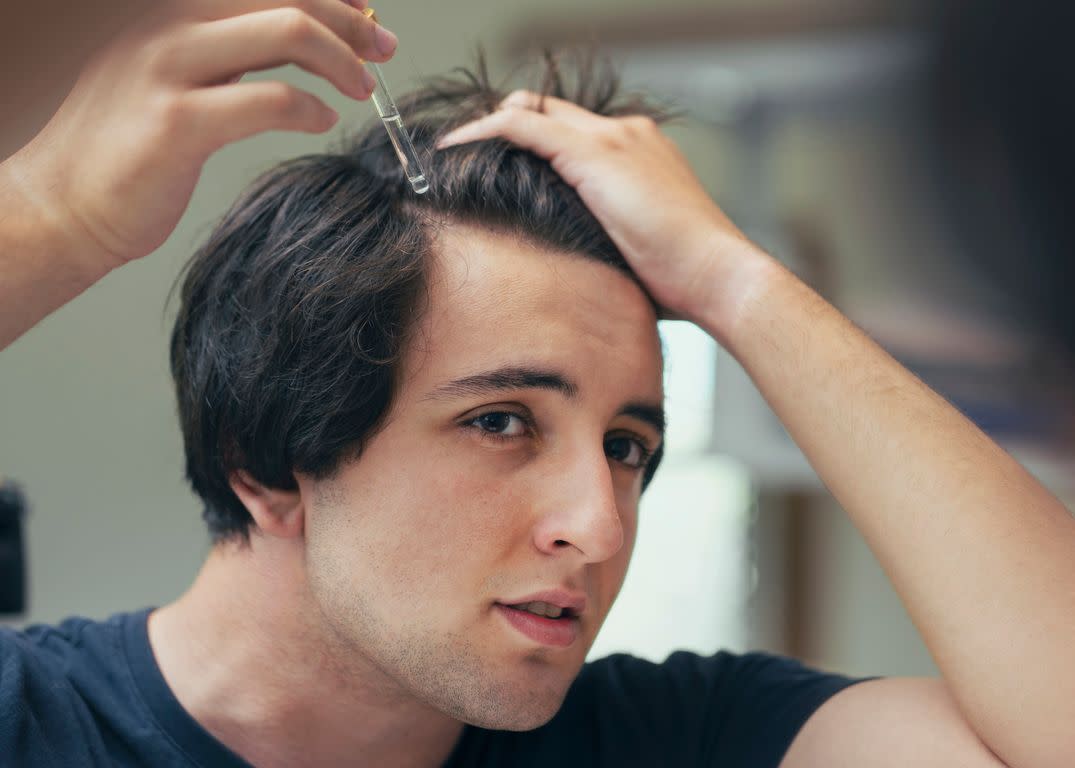 Young man dropping serum onto his hair