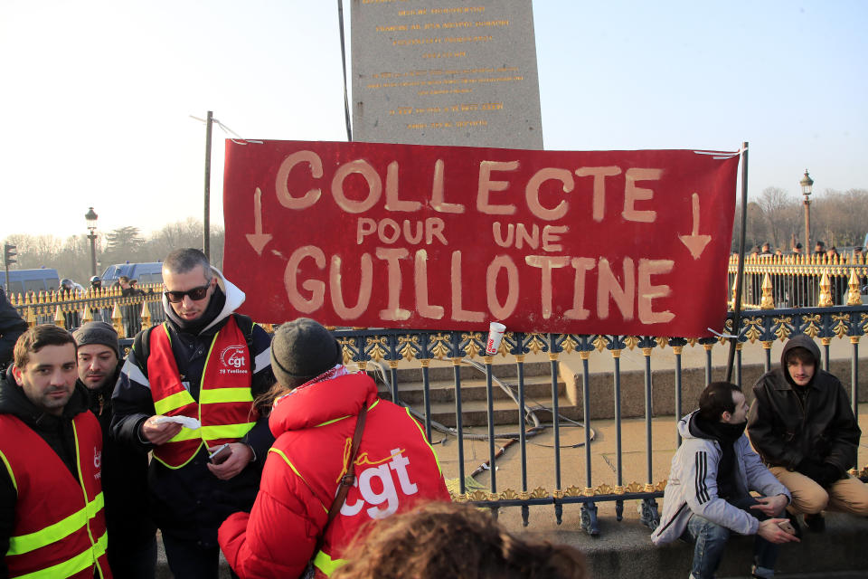 Unionists stand by a banner reading "Funds for a guillotine" on the Place de la Concorde during a demonstration, Friday, Jan. 24, 2020 in Paris. French unions are holding last-ditch strikes and protests around the country Friday as the government unveils a divisive bill redesigning the national retirement system. (AP Photo/Michel Euler)