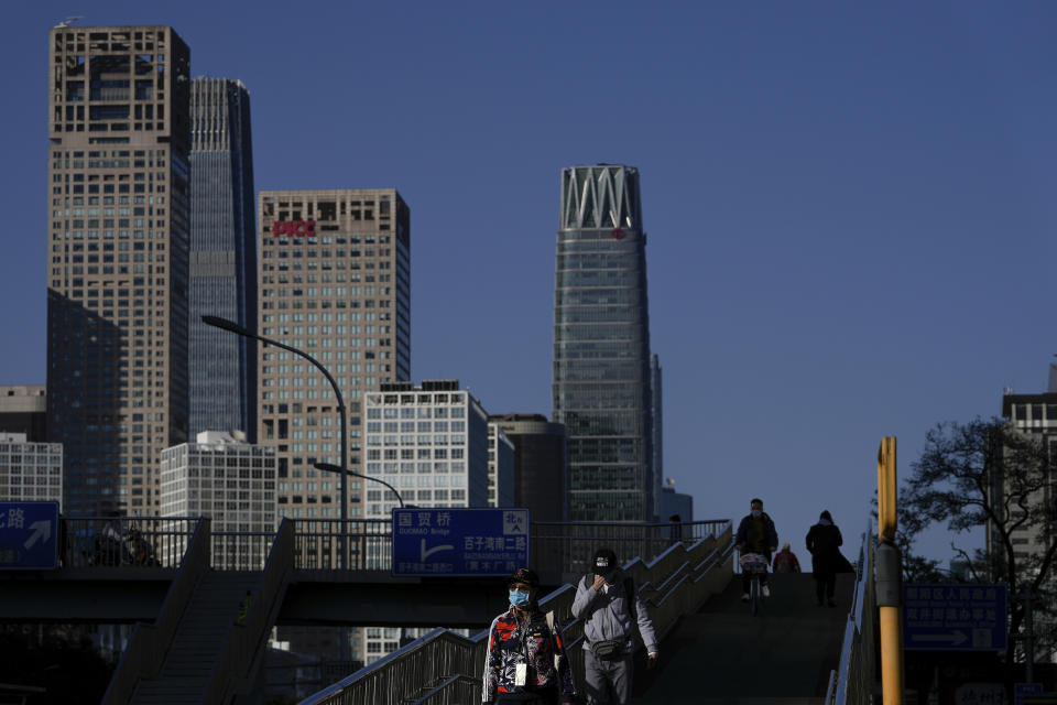 People wearing face masks walk on a pedestrian overhead bridge against the commercial office buildings in Central Business District in Beijing on Oct. 26, 2021. China’s economic rebound from the coronavirus pandemic is stalling as President Xi Jinping’s government cracks down on surging corporate debt. (AP Photo/Andy Wong)