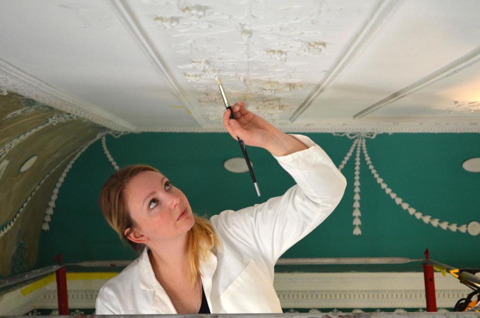 This undated handout photo provided by Mount Vernon shows Amelia Jensen working on New Room ceiling near the palladian window at George Washington's Mount Vernon, Va. estate. The keepers of Washington's Mount Vernon estate on Friday announced a major reinterpretation of the largest room in the Founding Father's riverfront mansion. For decades, interpreters showed the room to tourists as Washington's large dining room. Upon further review, historians at Mount Vernon have concluded that the room Washington referred to as the "new room" that was added at the start of the American Revolution was actually more of a multi-purpose salon to impress and entertain visitors. A yearlong reinterpretation of the New Room will be unveiled to the public on Saturday, with a more authentic paint scheme and dozens of artifacts that Washington himself kept in the room. (AP Photo/Mount Vernon)