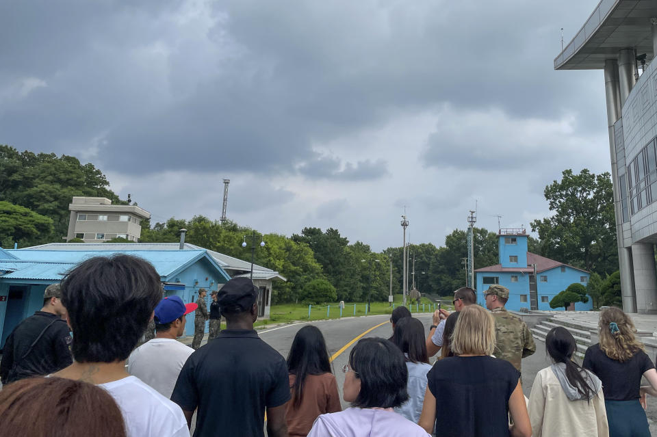 Un grupo de turistas permanece cerca de una estación fronteriza en la localidad de Panmunjom en la Zona Desmilitarizada, el martes 18 de julio de 2023, en Paju, Corea del Sur. La foto fue tomada poco antes de que el soldado estadounidense Travis King, de espalda con camisa azul oscura y gorra oscura, echara a correr y cruzara hacia Corea del Norte. (AP Foto/Sarah Jane Leslie)