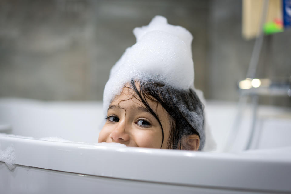 Kind spielt in der badewanne, schaut über rand mit schaum auf dem Kopf