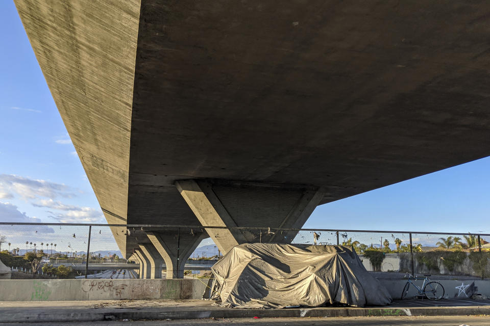 Homeless people camp under Interstate 110 in downtown Los Angeles on Friday, March 27, 2020. On Friday, California Gov. Gavin Newsom and Los Angeles Mayor Eric Garcetti said the surge in COVID-19 that health officials warned about will worsen. (AP Photo/Damian Dovarganes)