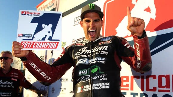 Indian Wrecking Crew member Jared Mees, celebrating in uniform as he holds up a finger on one hand and a 2017 champion banner in the other.