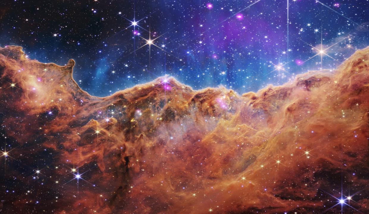 cosmic cliffs of the carina nebula red brown cliff-shaped clouds in blue starry space peppered with white and pink stars