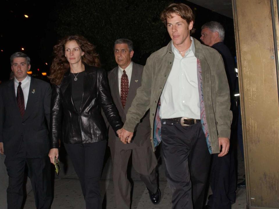 Julia Roberts, in an all-black outfit, walks out of a film screening while holding hands with husband Danny Moder, in a grey jacket, white shirt, and brown pants, in this photo from 2002.