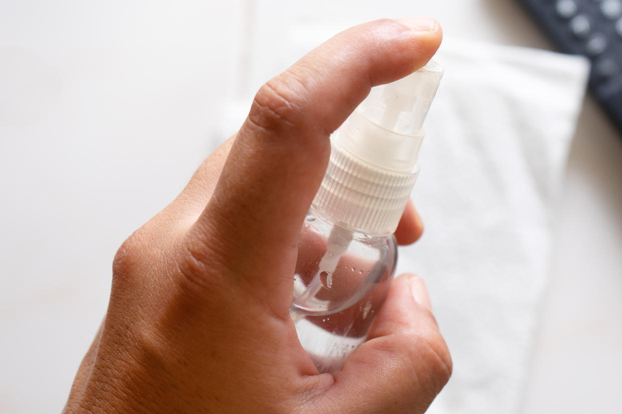 Cleaning tv remote control with disinfectant in plastic spray bottle on white background