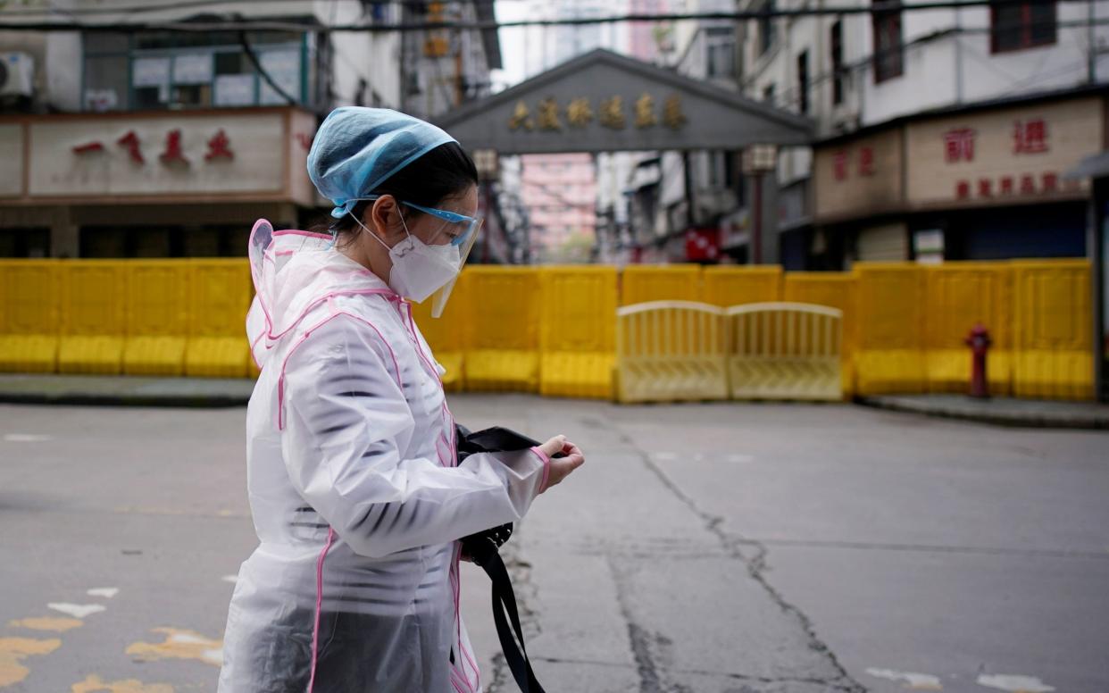 A woman wearing a face mask walks at a residential area blocked by barriers in Wuhan, the city where the coronavirus outbreak began - Aly Song/Reuters