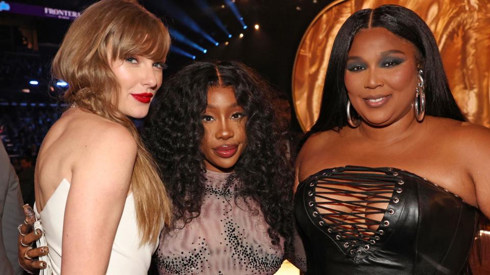 Taylor Swift, SZA and Lizzo at the 2014 Grammy's - Taylor is wearing a white dress, SZA is wearing a mauve top with sparkles and Lizzo is wearing a leather corset.