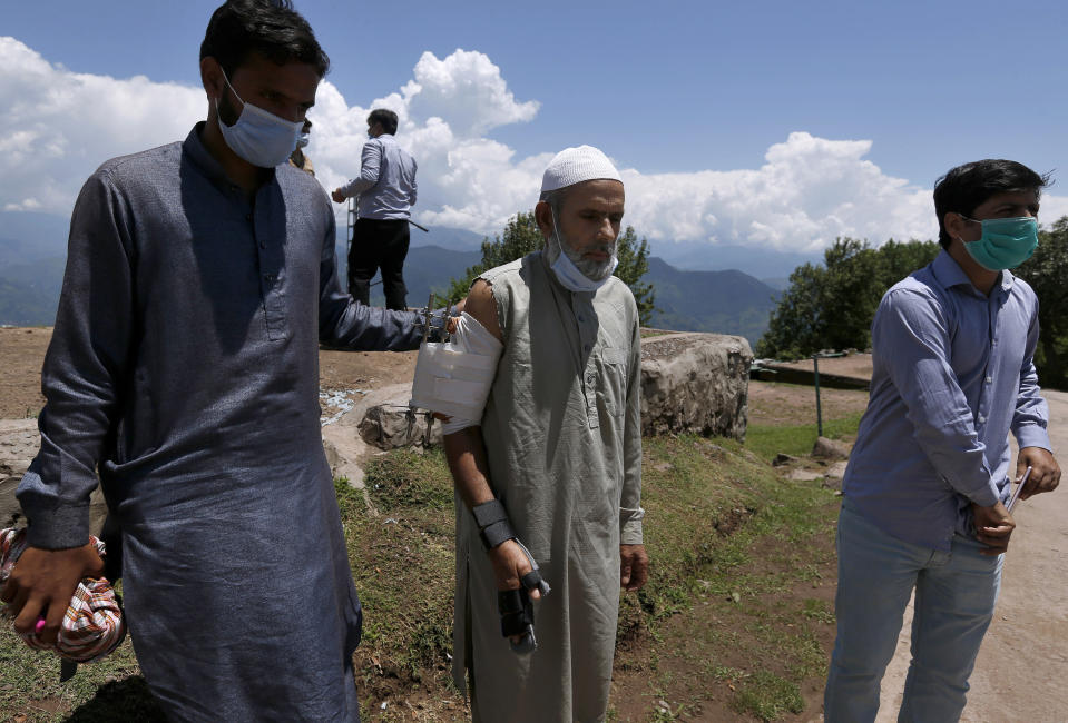 Abdul Aziz, center, who was injured when shrapnel from an Indian mortar wounded his arm, is helped by his son while he arrives to talk with journalists in Chiri Kot sector near Line of Control, that divides Kashmir between Pakistan and India, Wednesday, July 22, 2020. Villagers living along a highly militarized frontier in the disputed region of Kashmir have accused India of "intentionally targeting" civilians, but they are vowing that they would never leave their areas. Villagers say the fear of death is no longer present in their hearts after spending so many years in a state of shock and uncertainty. (AP Photo/Anjum Naveed)