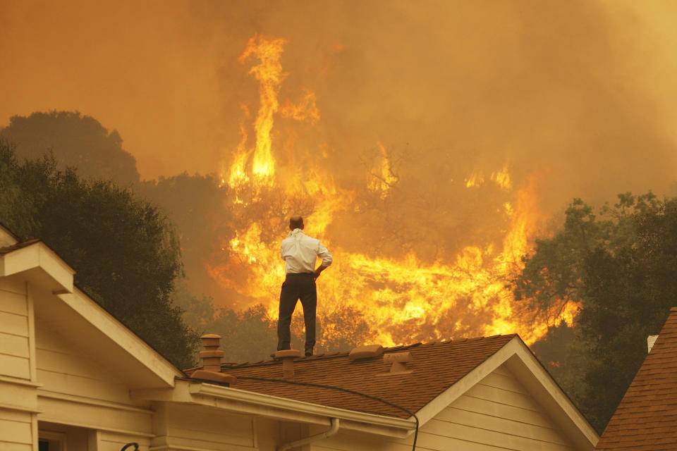 A man standing on his roof in California watching fires burning on a hill opposite.