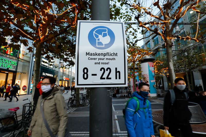 Pedestrians walk past a sign that reminds to wear a face mask, in Frankfurt