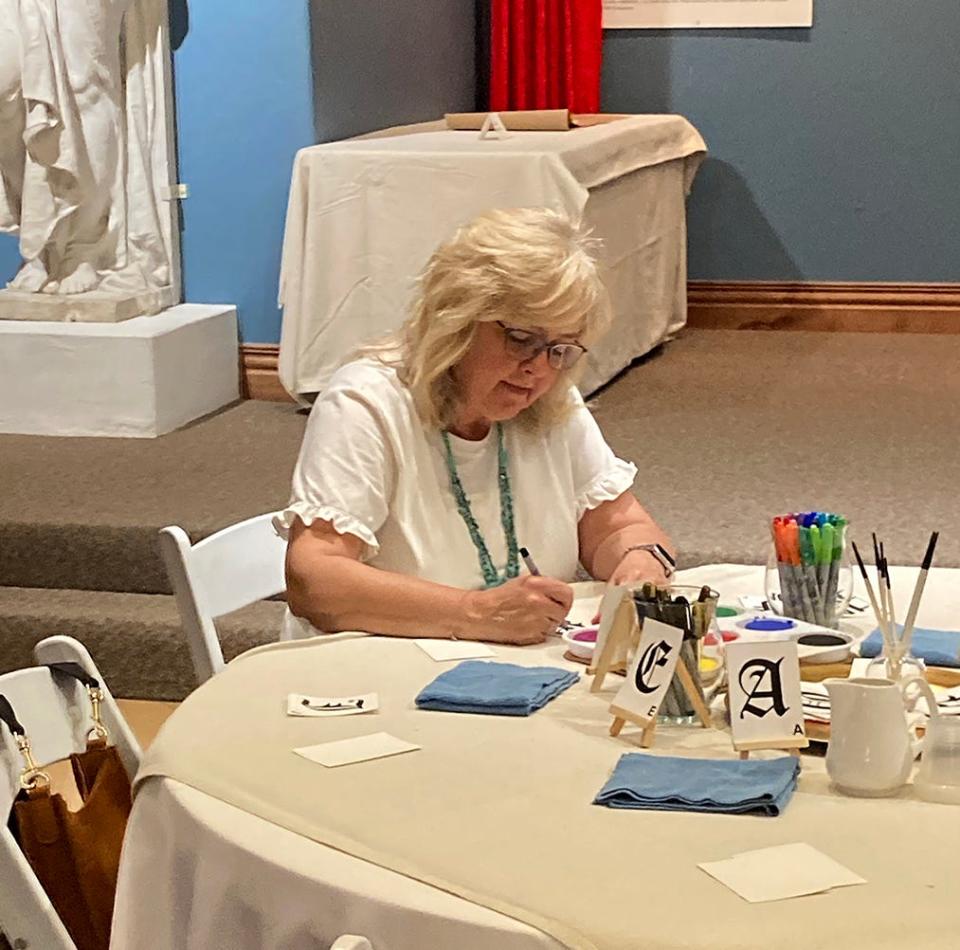 Kathy Haynes tries decorating a large initial letter at the hands-on portion of the “Painted Pages” exhibit at Canadian’s Citadelle Art Museum.