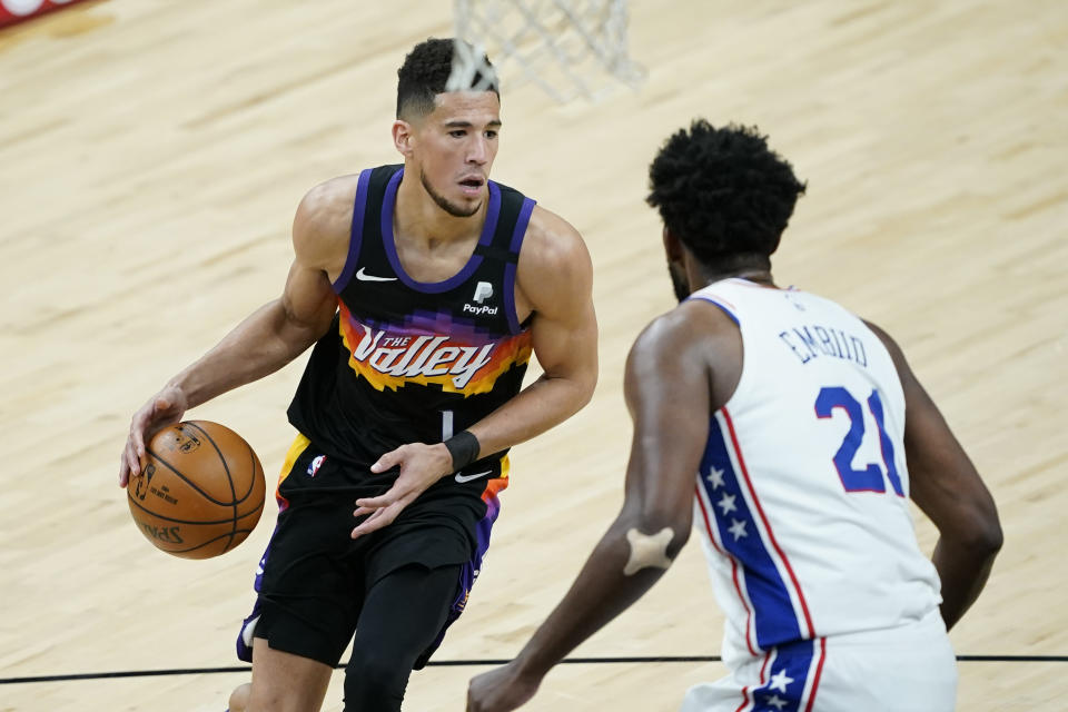 Phoenix Suns guard Devin Booker (1) looks to pass as Philadelphia 76ers center Joel Embiid (21) defends during the second half of an NBA basketball game, Saturday, Feb. 13, 2021, in Phoenix.(AP Photo/Matt York)