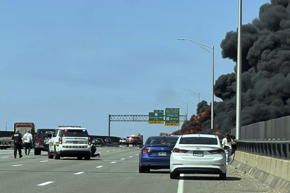 This photo provided by Angelique Feliciano shows firefighters and police responding after a crash involving a fuel truck and a car sparked a fire on the Gold Star Bridge between New London and Groton, Conn., on Friday, April 21, 2023. The crash closed Interstate 95 in both directions during the blaze. (Angelique Feliciano via AP)