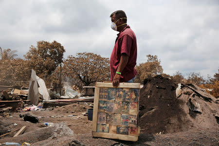 A resident holds framed pictures of his family, recovered from his house in an area affected by the eruption of the Fuego volcano, in San Miguel Los Lotes, in Escuintla, Guatemala June 13, 2018. REUTERS/Luis Echeverria