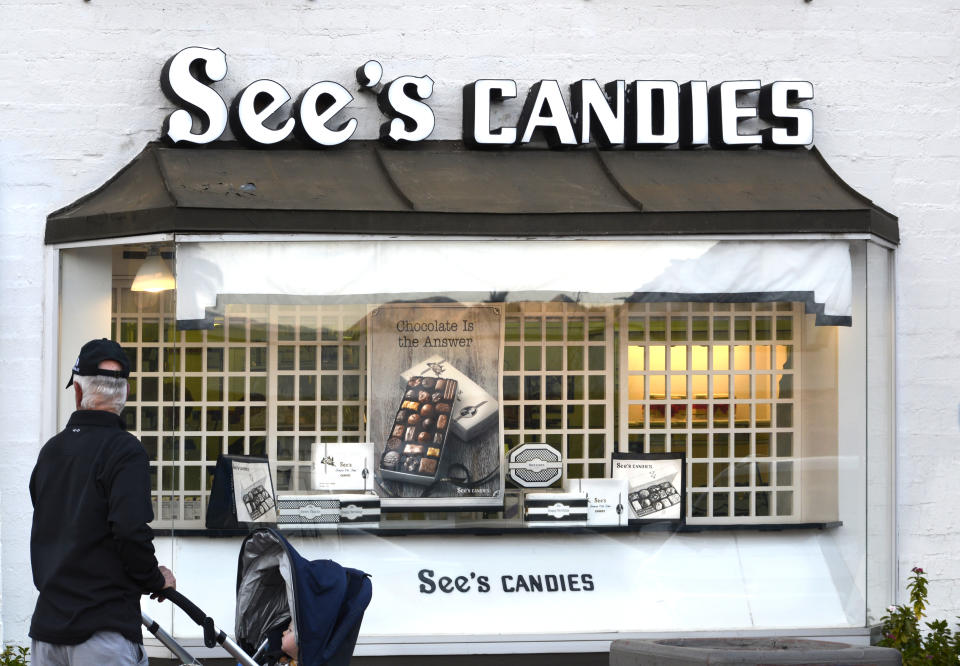 PALM SPRINGS, CALIFORNIA - FEBRUARY 25, 2019: A man pushing a baby carriage pauses in front of a See's Candies shop in Palm Springs, California. Founded in Los Angeles in 1921, the company is now headquartered in San Francisco, California. Since 1972 the company has been owned by Warren Buffett's Berkshire Hathaway Corporation. (Photo by Robert Alexander/Getty Images)