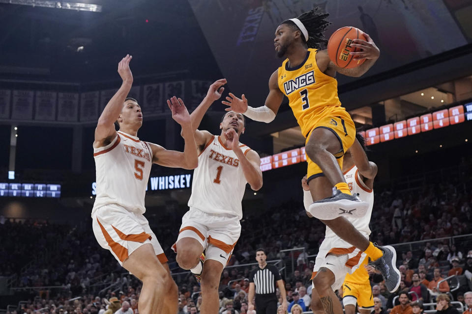 UNC Greensboro guard Kobe Langley (3) looks to pass past the ball past Texas forward Kadin Shedrick (5) and forward Dylan Disu (1) during the first half of an NCAA college basketball game in Austin, Texas, Friday, Dec. 29, 2023. (AP Photo/Eric Gay)