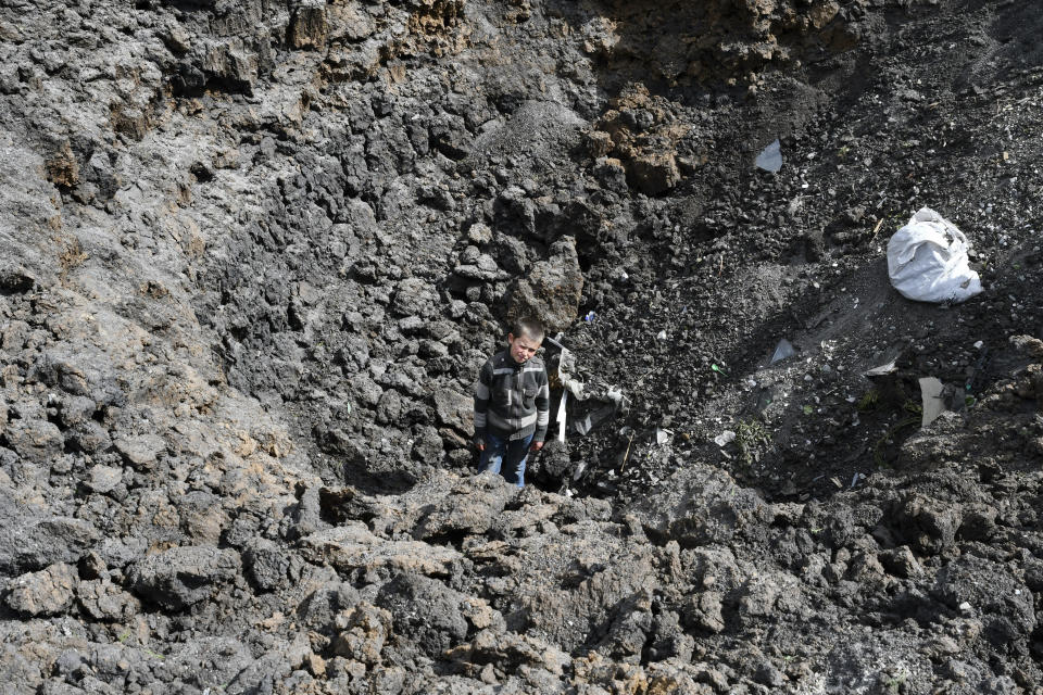 Maxim stands in the crater of an explosion after Russian shelling next to the Orthodox Skete in honor of St. John of Shanghai in Adamivka, near Slovyansk, Donetsk region, Ukraine, Tuesday, May 10, 2022. (AP Photo/Andriy Andriyenko)