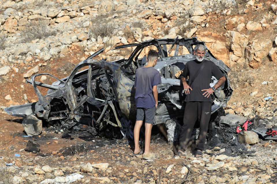 People stand next to the damaged car that hit by an Israeli airstrike in the town of Ainata, a Lebanese border village with Israel in south Lebanon, Monday, Nov. 6, 2023. An Israeli airstrike in south Lebanon on Sunday, Nov. 5, 2023 evening killed four civilians, including a woman and three children, raising the likelihood of a dangerous new escalation in the conflict on the Lebanon-Israel border. (AP Photo/Mohammed Zaatari)