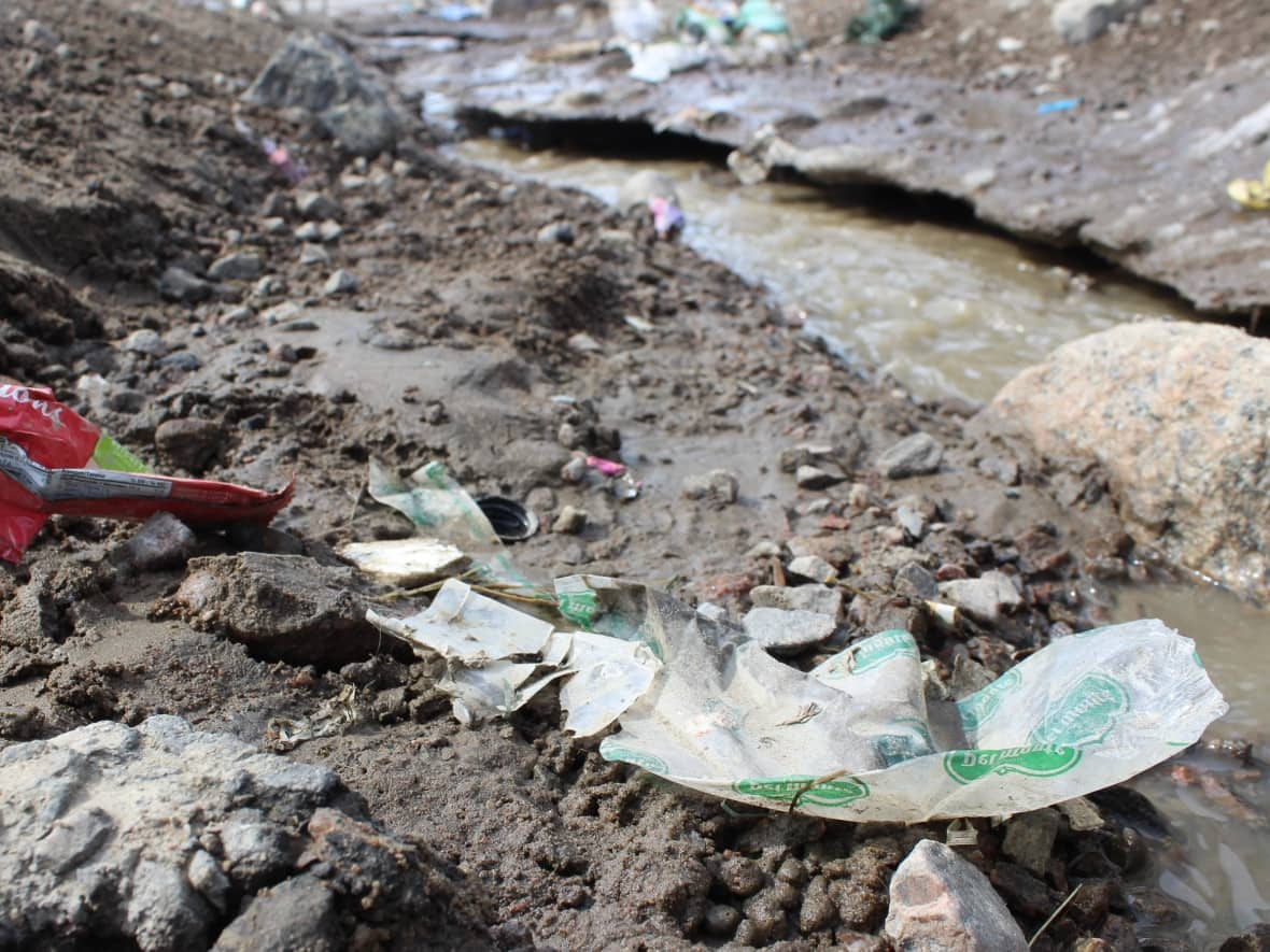 Plastic packaging lies in a ditch along Queen Elizabeth Street in Iqaluit on May 9, 2022. Billy Merkosak, a hunter in Pond Inlet, says he's seen plastic inside the bellies of Arctic char — and one of the changes he'd like to see, to try and curb the problem, is less plastic packaging in grocery stores. (Liny Lamberink/CBC - image credit)