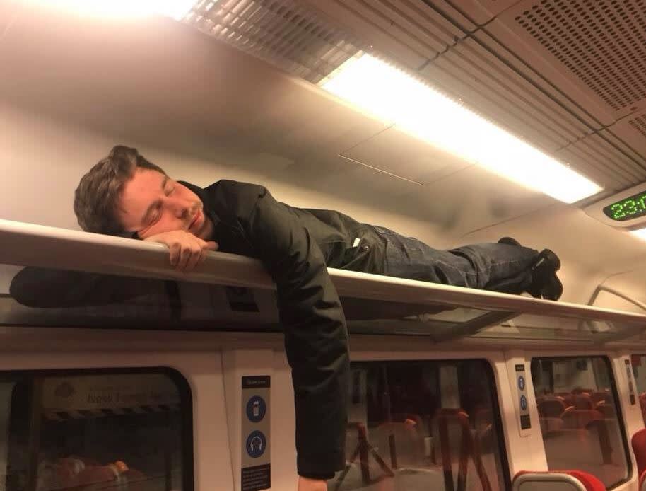 A passenger stuck overnight on the London Waterloo to Bournemouth train tries to sleep in an overhead compartment (Samantha Blackburn)