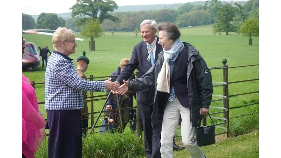 Princess Anne wearing two scarves and shaking hands with a woman